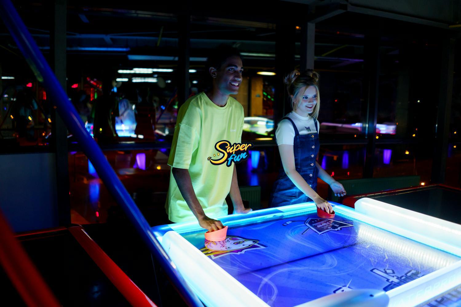 A young man and woman playing air hockey in a brightly lit arcade. A young man and woman playing air hockey in a brightly lit arcade.
