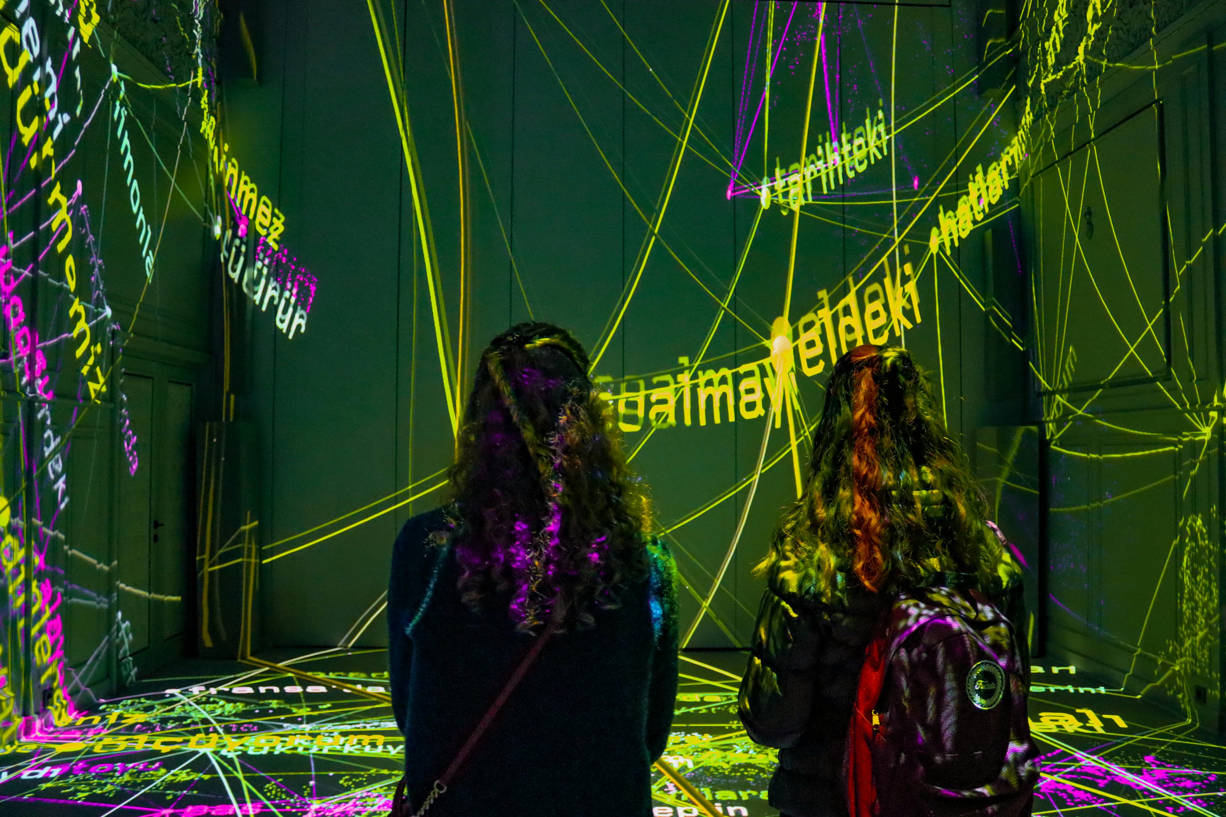People view Interactive Projection Mapping art with colorful lights and words.