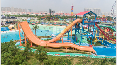 Aerial view of a vibrant water park with orange slides, pools, and city buildings in distance.