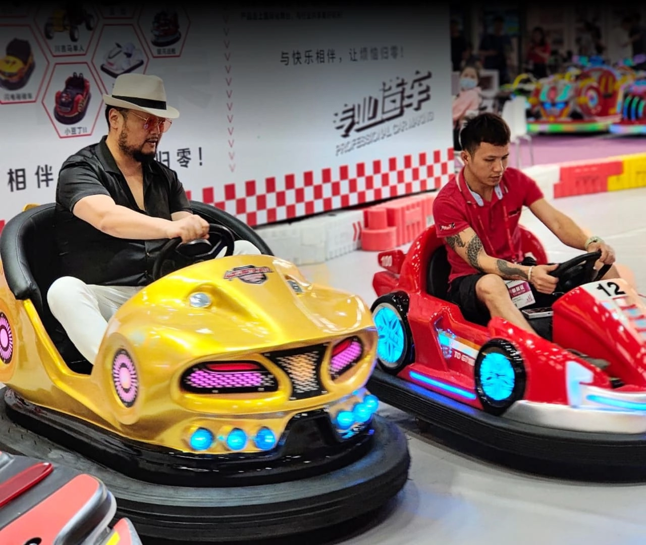 Two people are driving bumper cars, one in a gold car and one in a red car. They are on a race track.