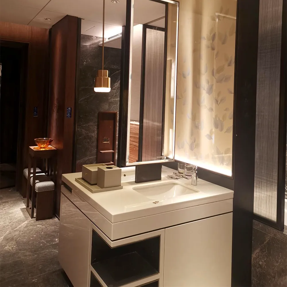 Completed bathroom vanity in luxury hotel room white Corian sink, backlit mirror, dark marble walls, and brass pendant light.