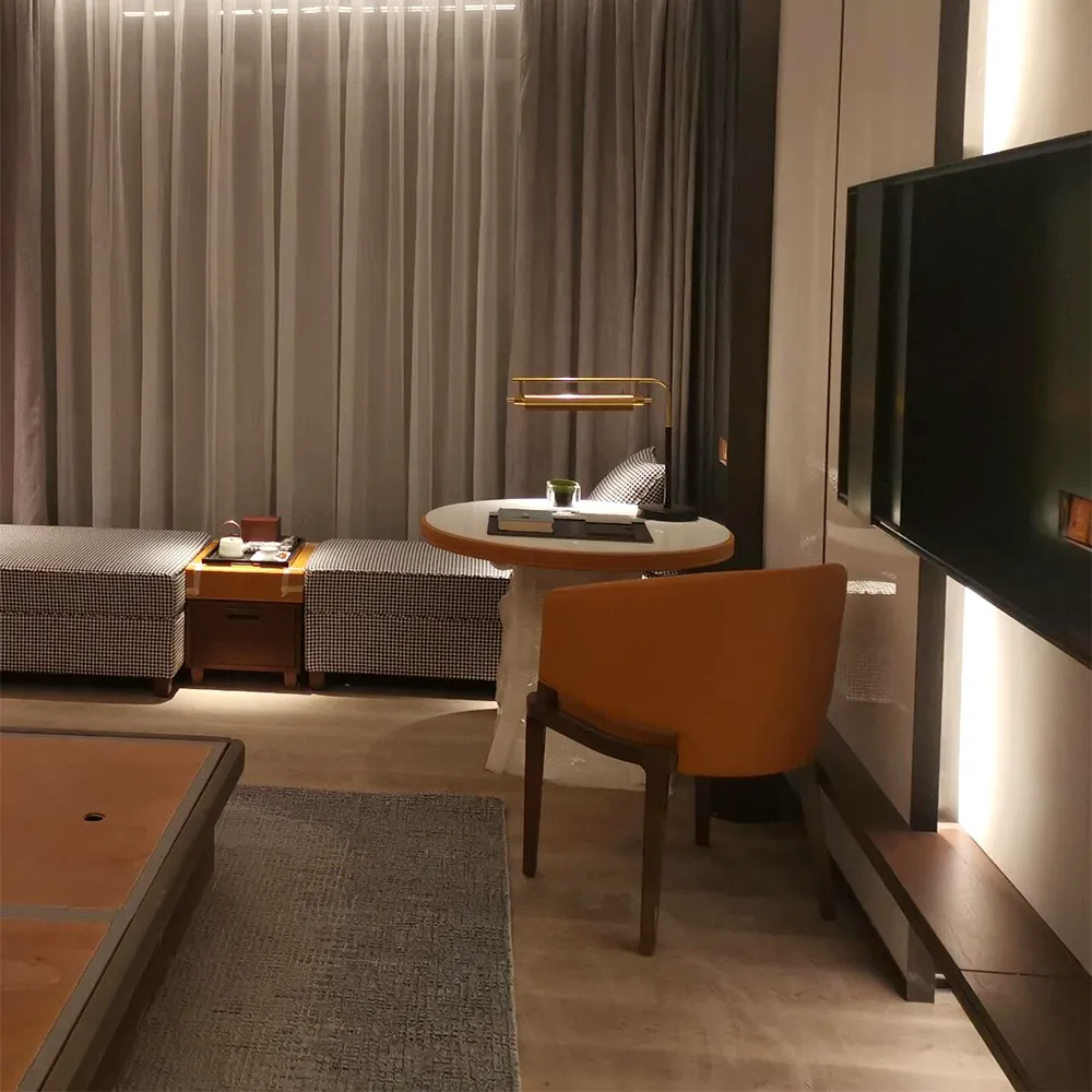 Finished hotel guestroom lounge with houndstooth ottomans, round marble desk, amber leather chair, and ambient backlighting.