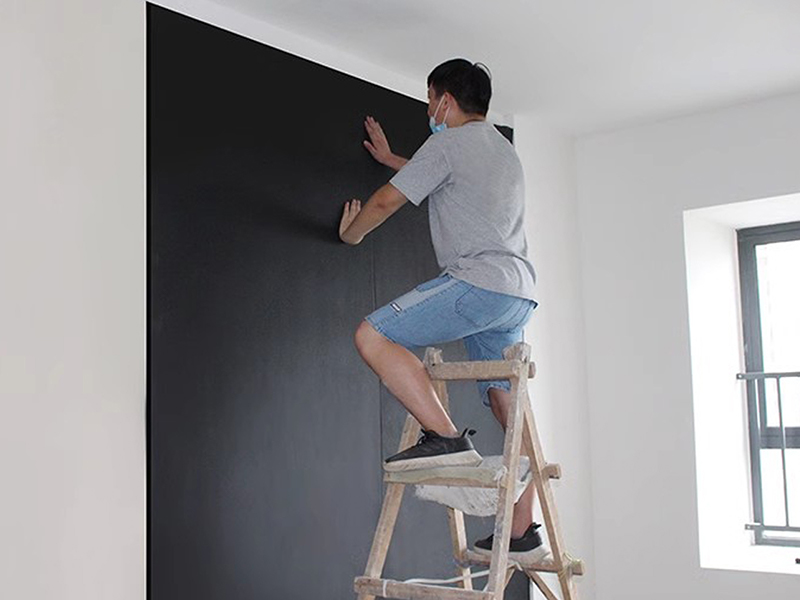 Man installing black rubber insulation sheet on wall.