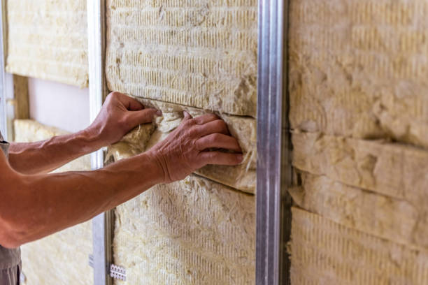 Hands installing rock wool board insulation in a wall.