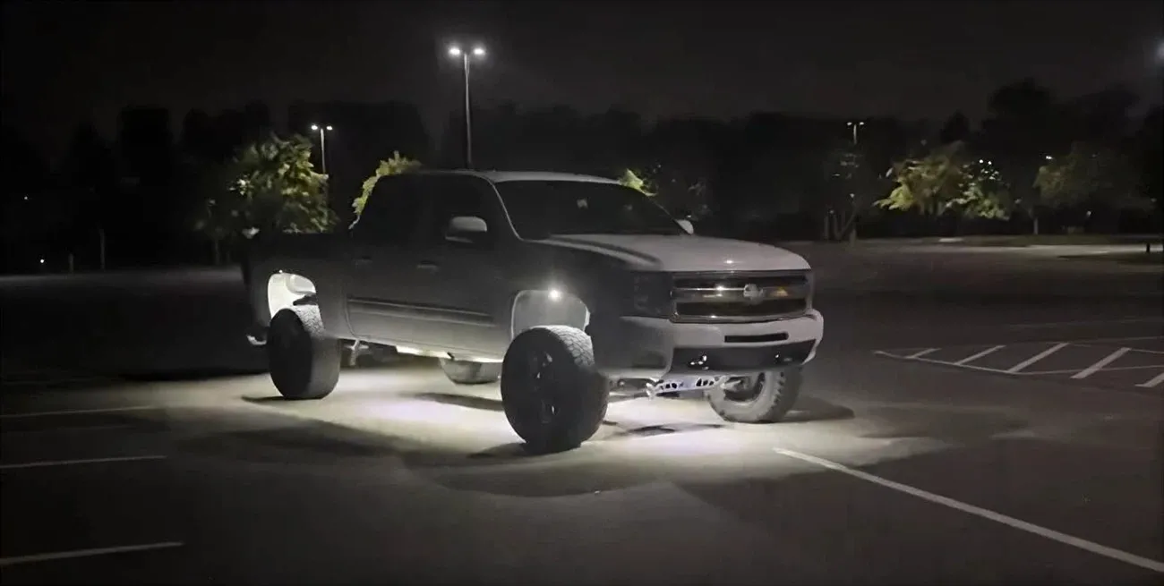 White lifted Chevrolet pickup truck with illuminated rock lights in a nighttime parking lot