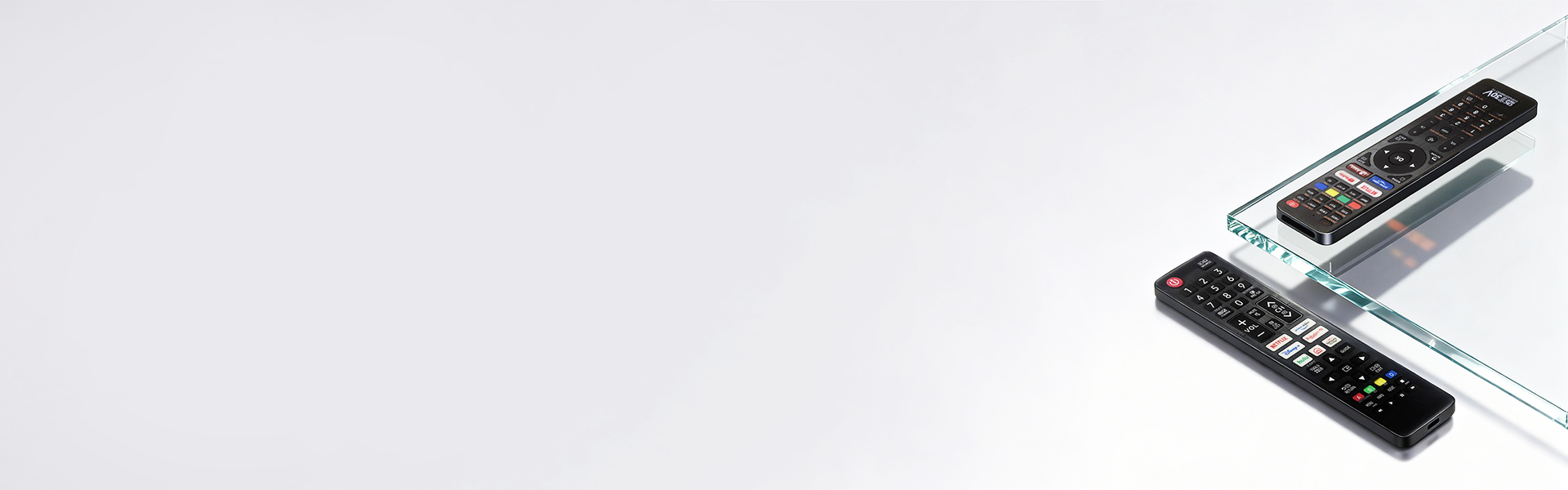 Two black TV remotes on a clear glass surface against a white background. - SYSTO