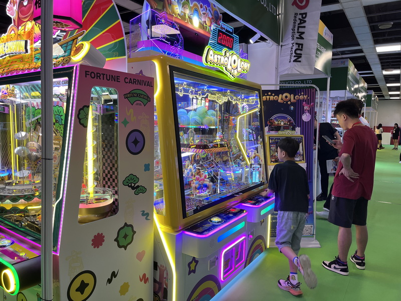 Visitor testing a PALM FUN redemption arcade game as an adult observes gameplay at the GTI Southeast Asia Expo