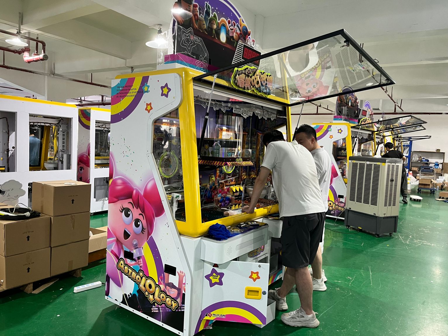 Two PALM FUN factory technicians working on a coin pusher arcade cabinet during equipment preparation