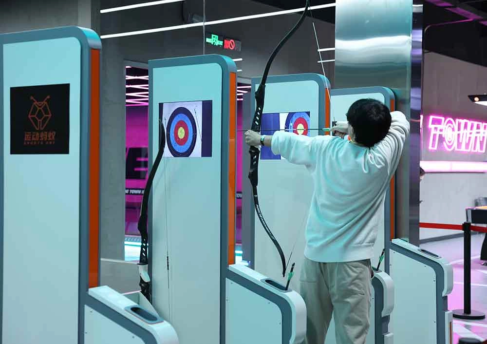 A man is using a bow and arrow to shoot at a target on an archery target simulator.