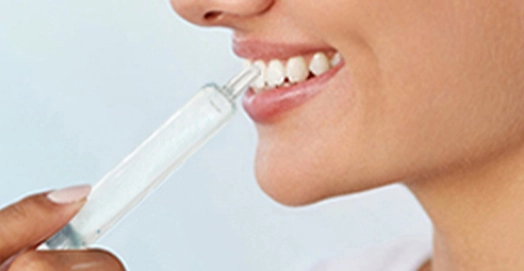 Close-up of a woman applying a teeth whitening gel to her teeth.