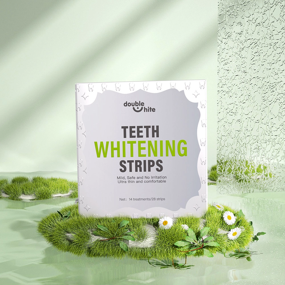 Une boîte de bandes blanchissantes pour les dents Double White. La boîte est blanche avec un texte vert et une image d&#39;une bouche souriante avec des dents blanches sur le devant. La boîte est posée sur une surface herbeuse verte avec des fleurs blanches.