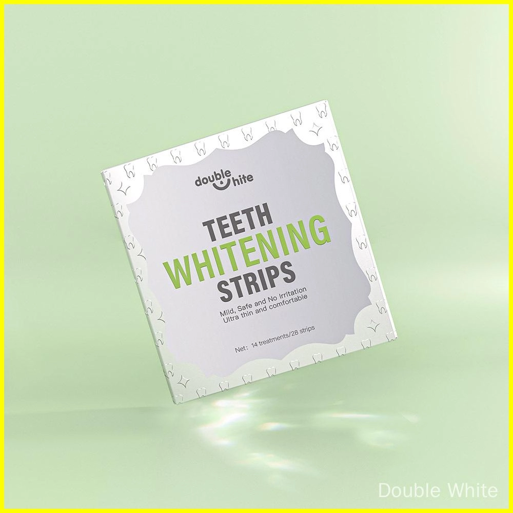 Une boîte de bandes de blanchiment des dents Double White. La boîte est blanche avec un texte vert et un motif de feuille verte. La boîte est posée sur un fond vert uni.
