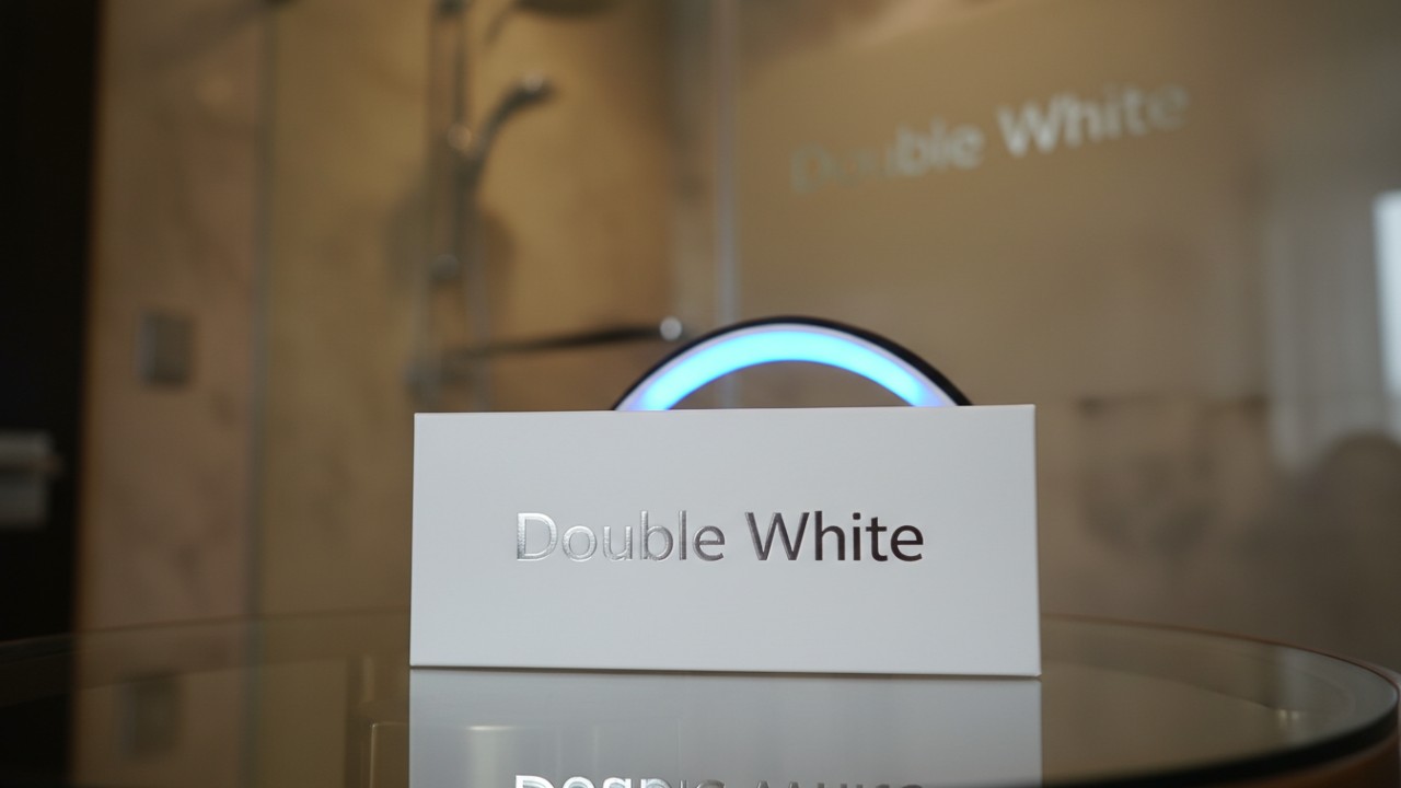 Gros plan luxueux du kit de blanchiment Double White et de son appareil LED sur une surface en verre avec logo argenté en relief.