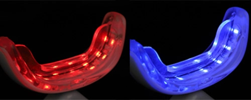 Imagen en primer plano de dos dispositivos de blanqueamiento dental con luz LED. El dispositivo de la izquierda es rojo y el de la derecha es azul.