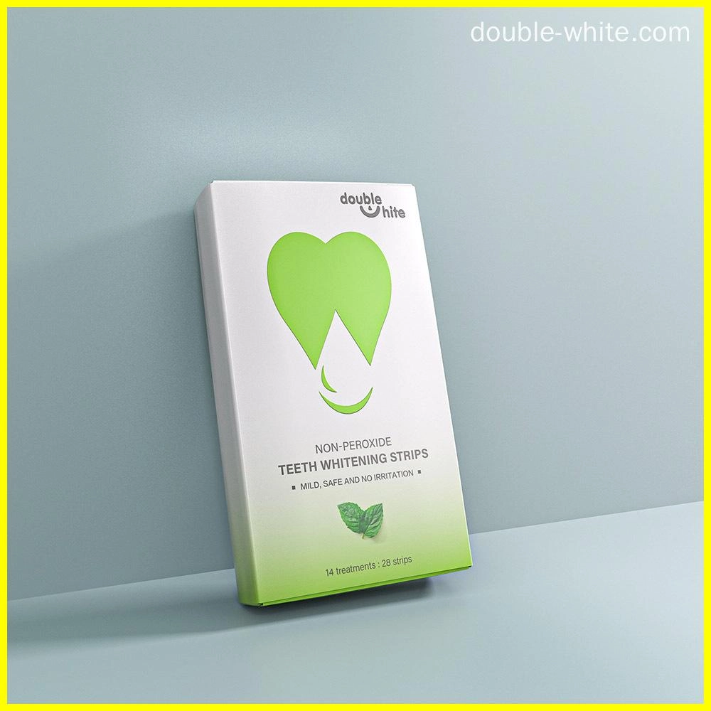 A box of Double White non-peroxide teeth whitening strips. The box is white with a green heart-shaped logo and green text. The box is sitting on a white surface against a pale blue background.