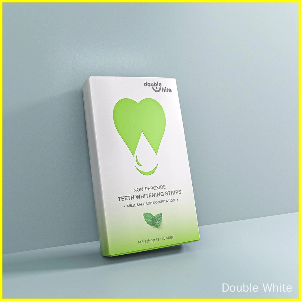Une boîte de bandes de blanchiment des dents sans peroxyde Double White. La boîte est blanche avec un logo vert en forme de cœur et un texte vert. La boîte est posée sur une surface blanche sur un fond bleu pâle.