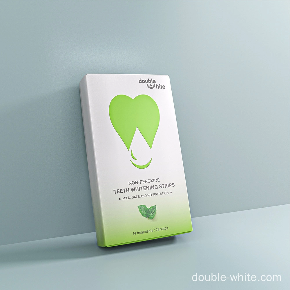 Безопасные полоски для отбеливания зубов Double White Коробка полосок для отбеливания зубов Double White без перекиси. Белая коробка с зелёным логотипом в форме сердца и зелёным текстом. Коробка стоит на белой поверхности на бледно-голубом фоне. - Double White