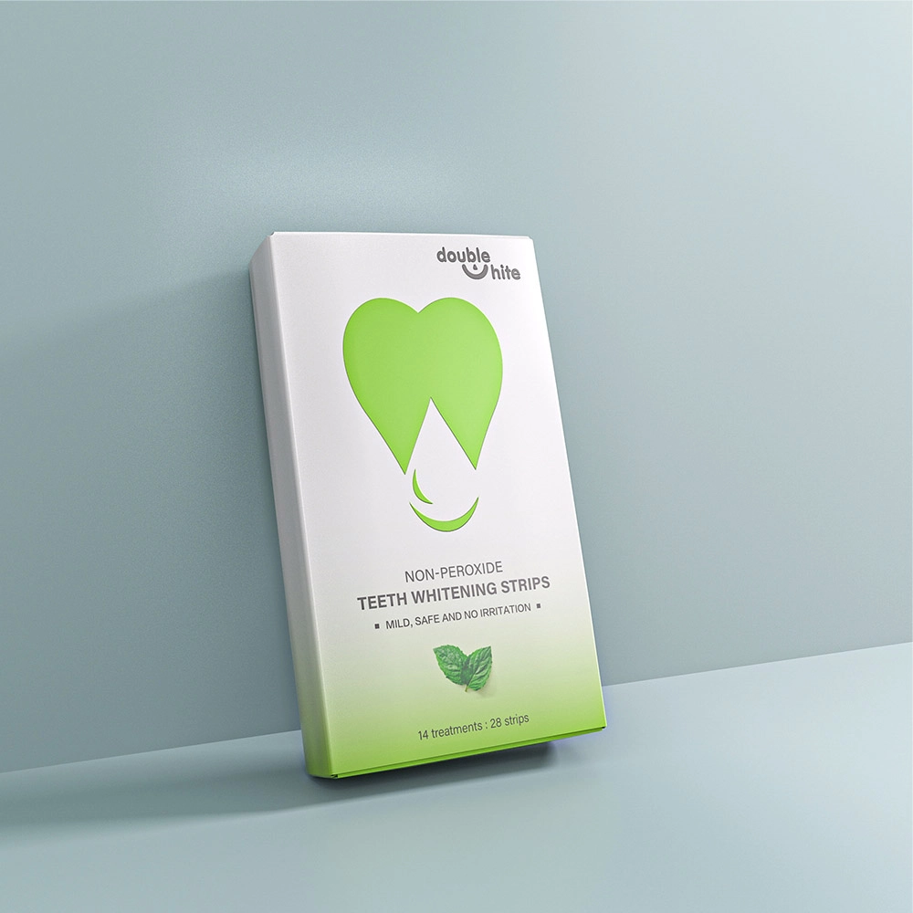 A box of Double White non-peroxide teeth whitening strips. The box is white with a green heart-shaped logo and green text. The box is sitting on a white surface against a pale blue background.