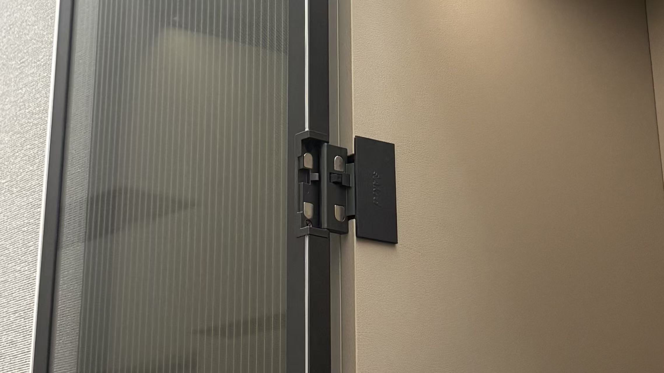 Close-up of a black metal hinge on a fluted glass cabinet door.