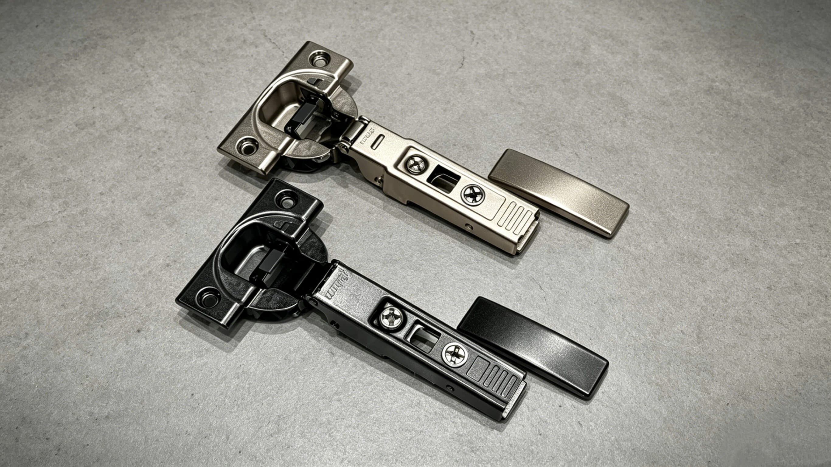 Two concealed cabinet hinges in nickel and black finishes on a gray surface. (1)