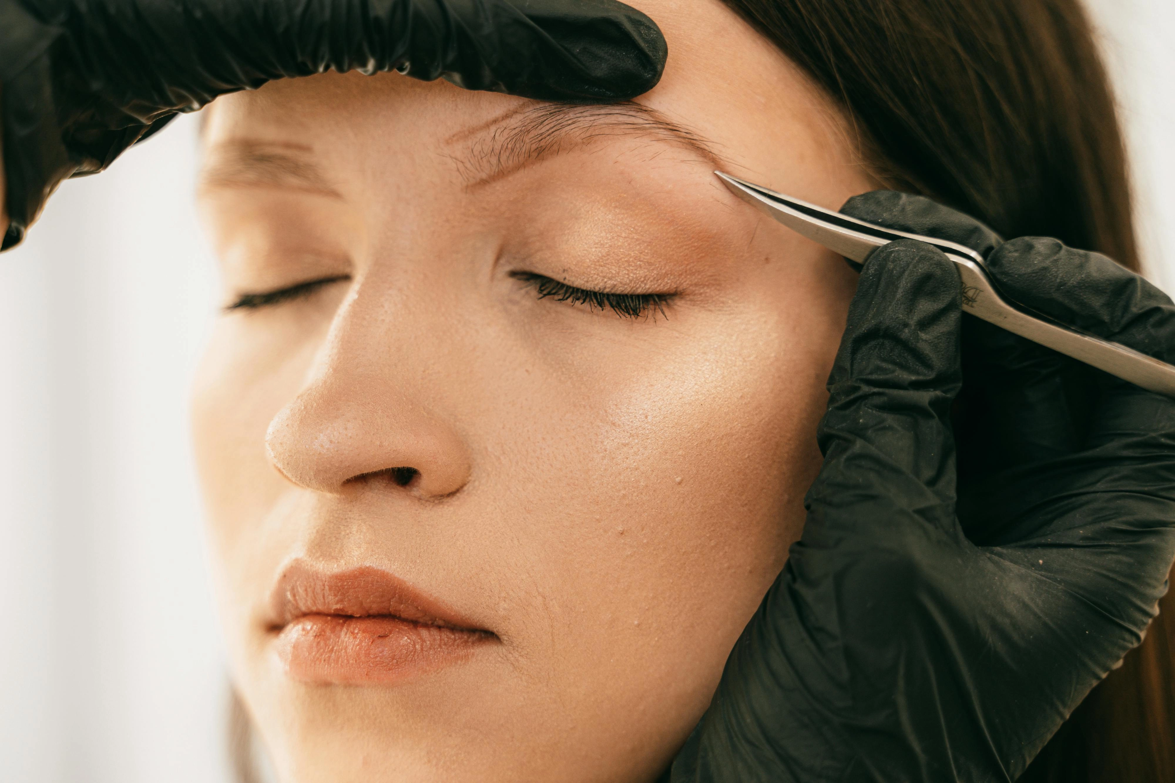Detailed-image-of-woman-getting-eyebrows-plucked-with-tweezers-by-a-beautician-wearing-gloves. Detailed image of woman getting eyebrows plucked with tweezers by a beautician wearing gloves.
