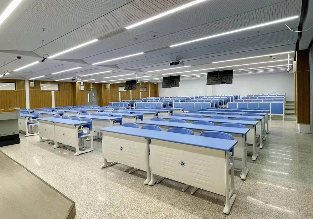 Modern lecture hall with rows of light blue student desks and chairs under bright fluorescent lighting.
