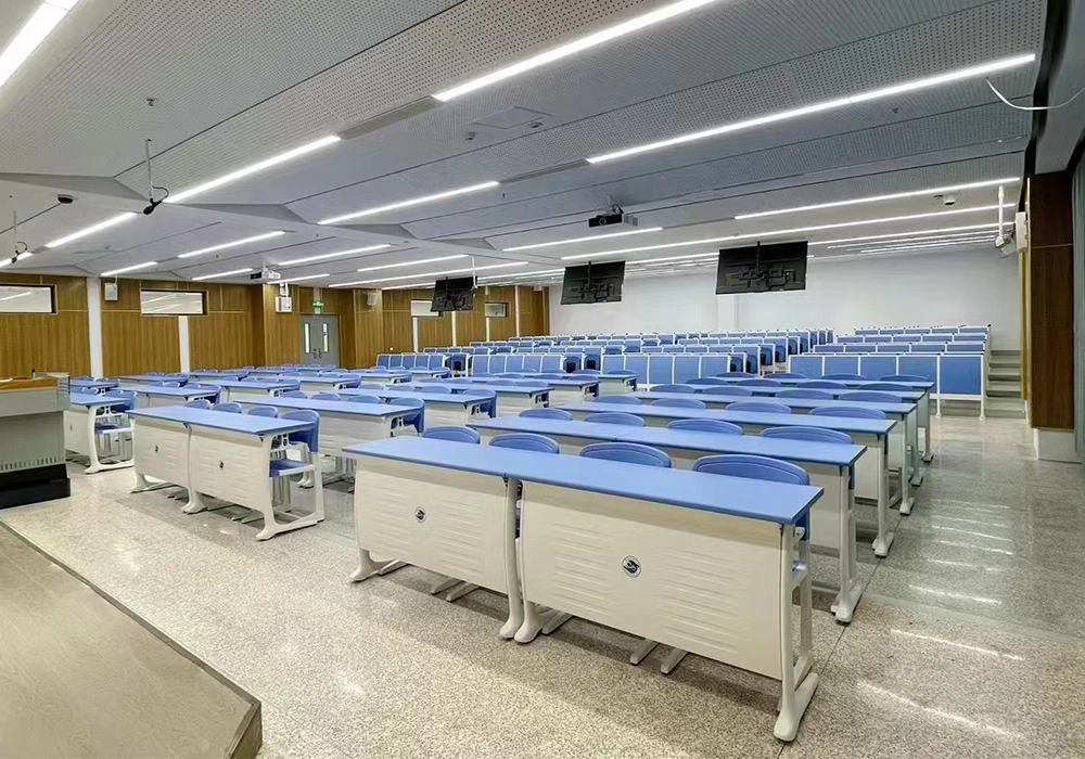 Modern lecture hall with rows of light blue student desks and chairs under bright fluorescent lighting.