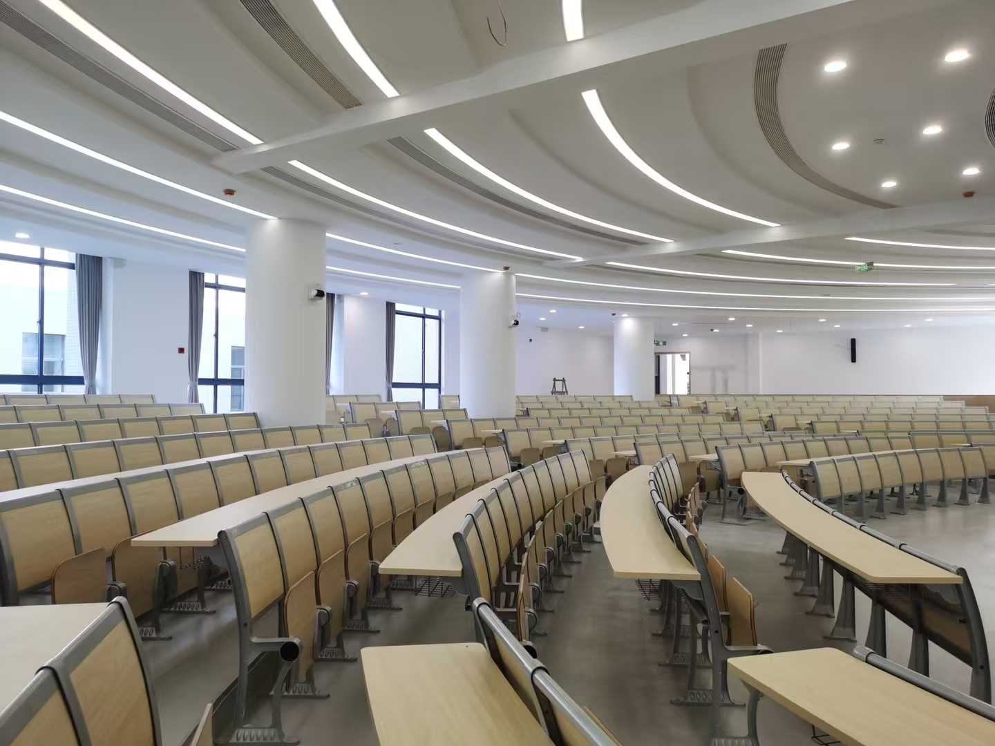 Modern university lecture hall with curved rows of light wood desks and chairs.