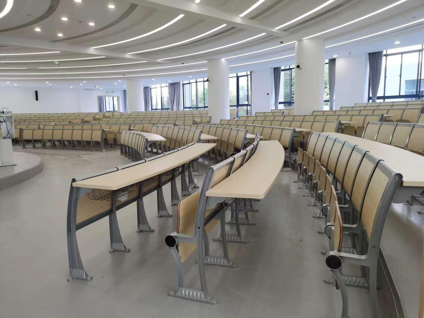 public-auditorium-chair Modern lecture hall with curved rows of light wood student desks and chairs.
