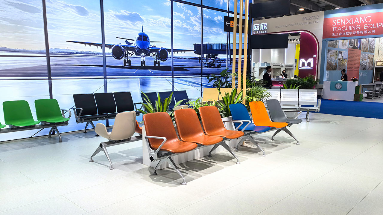 Rows of colorful airport-style seating are displayed at a trade show booth with an airplane backdrop.