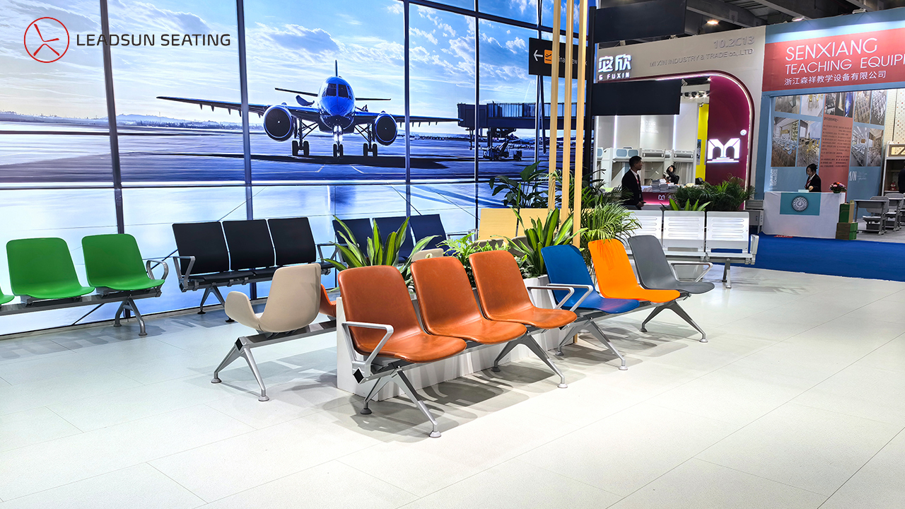 Rows of colorful airport-style seating are displayed at a trade show booth with an airplane backdrop. Rows of colorful airport-style seating are displayed at a trade show booth with an airplane backdrop.