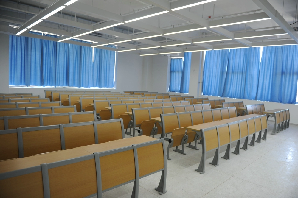 Empty-lecture-hall-with-light-wood-desks-and-chairs,-and-light-blue-curtains-on-the-windows. Empty lecture hall with light wood desks and chairs and light blue curtains on the windows.