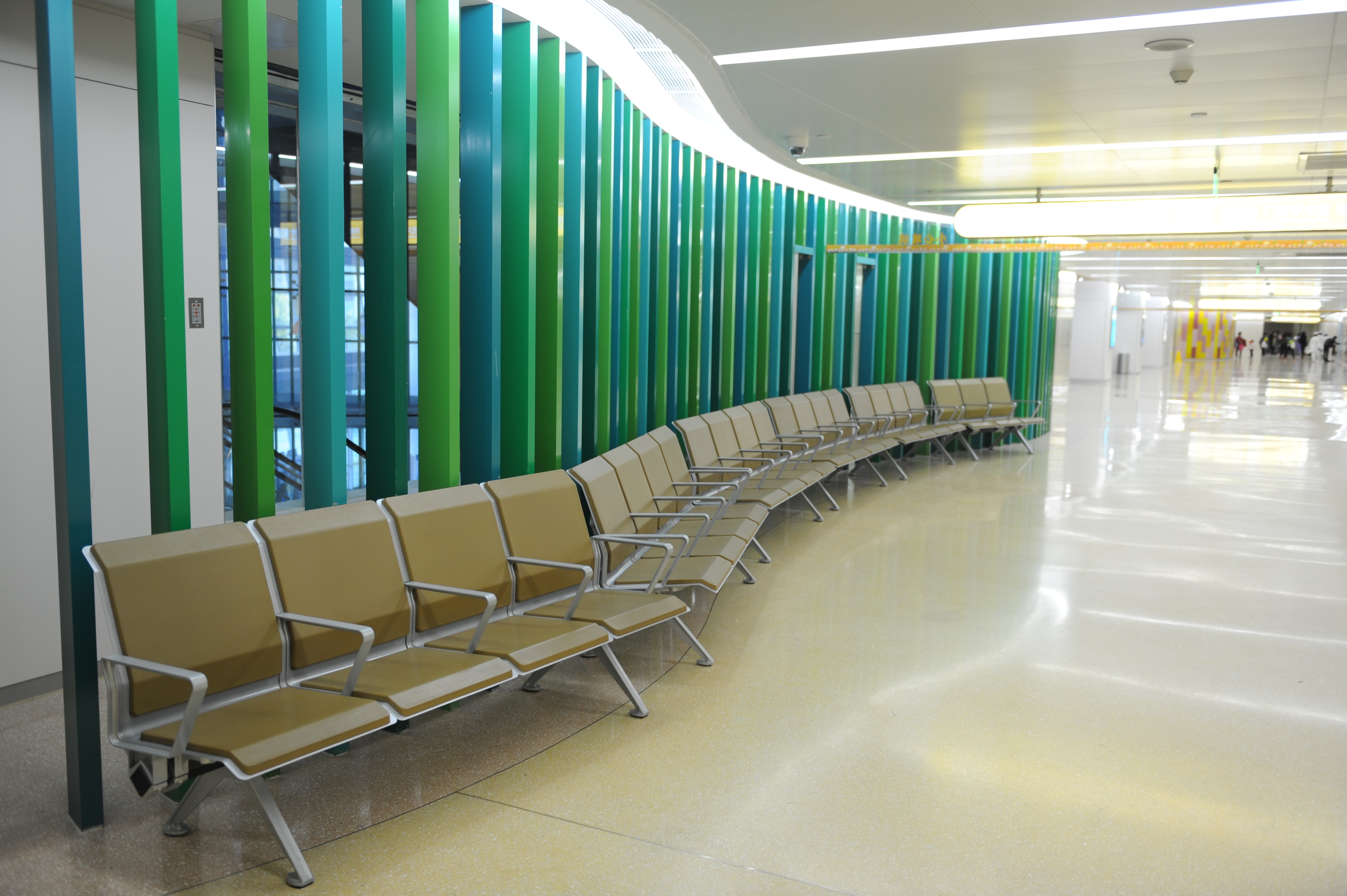 Empty tan chairs with silver frames in a modern airport waiting area with a green and teal striped wall.