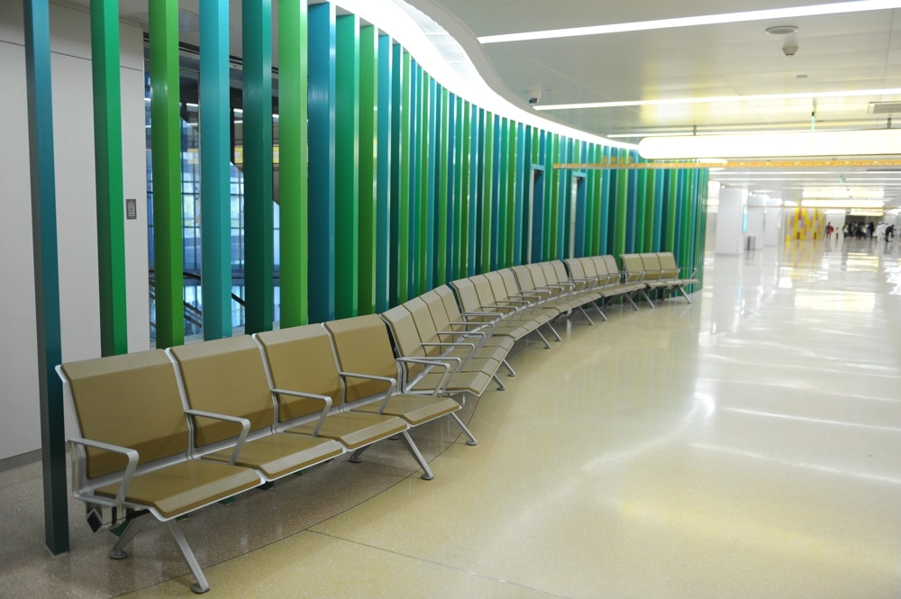 Modern-airport-waiting-area-with-tan-chairs-and-a-vibrant-green-and-teal-slatted-wall. Modern airport waiting area with tan chairs
