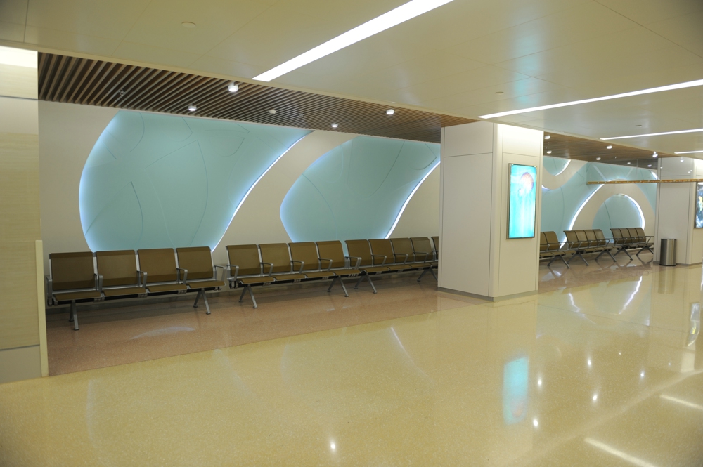 Modern waiting area with light beige tiled floor, pale blue wall art, and rows of brown metal and fabric waiting chairs. Modern waiting area with light beige tiled floor, pale blue wall art, and rows of brown metal and fabric waiting chairs.