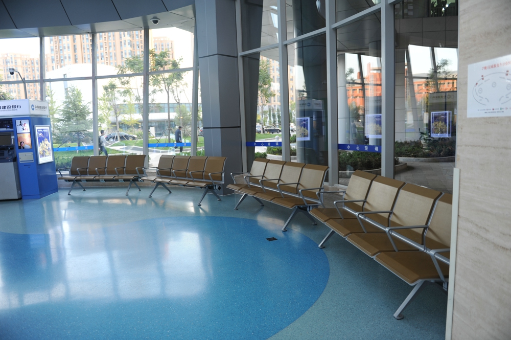 Modern waiting area with tan metal and upholstered seating arranged in two rows facing each other, ATM, and large windows overlooking a city street. Modern waiting area with tan metal and upholstered seating arranged in two rows facing each other, ATM, and large windows overlooking a city street.