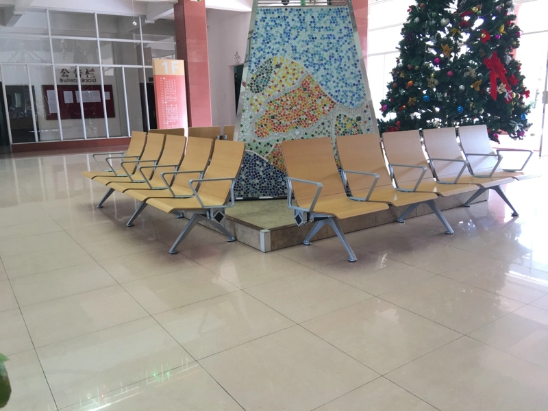 aluminum-die-cast-chairs Light beige waiting room chairs arranged in a row near a colorful mosaic wall and a decorated Christmas tree.