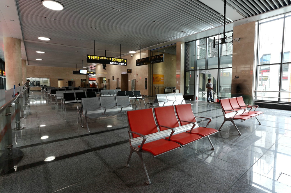 Modern waiting area with rows of gray and red metal seating, directional signage in Chinese, and large windows overlooking an exterior scene. Modern waiting area with rows of gray and red metal seating, directional signage in Chinese, and large windows overlooking an exterior scene.