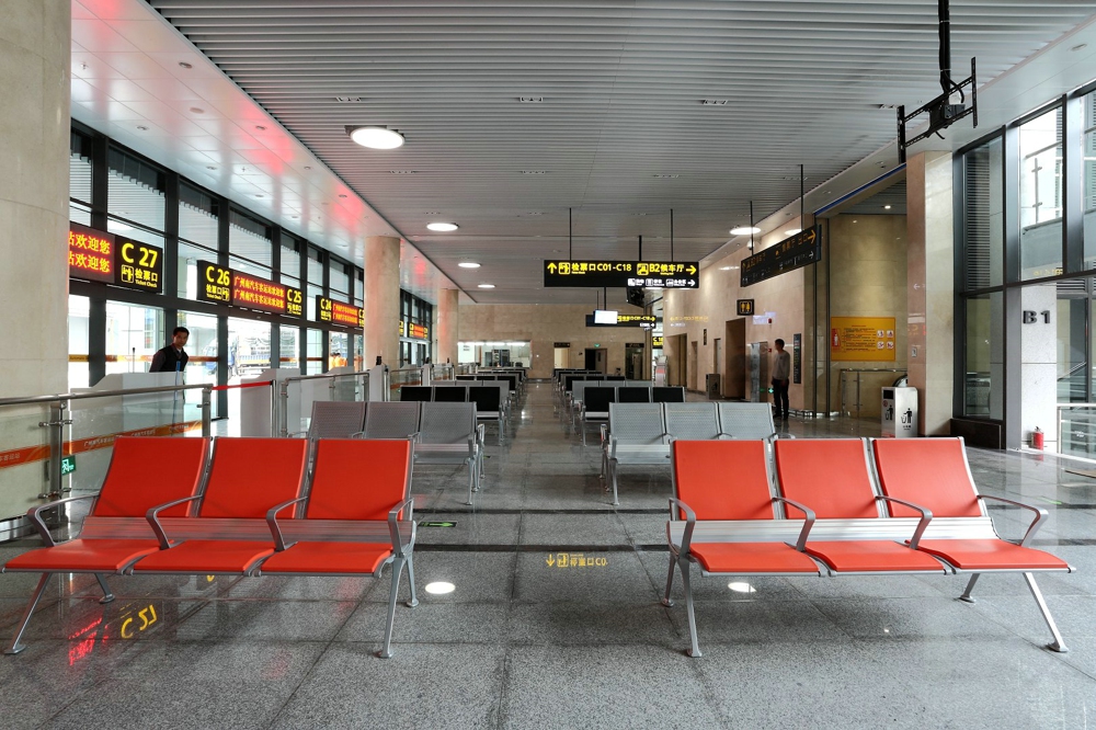 Waiting area in a modern transit station with rows of orange chairs and signage in Chinese indicating gate numbers and directions. Waiting area in a modern transit station with rows of orange chairs and signage in Chinese indicating gate numbers and directions.