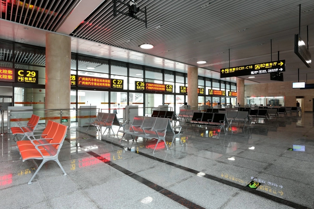 Empty-waiting-area-in-a-modern-transportation-terminal-with-orange-chairs-and-digital-signs-indicating-gates-C21-C29-and-directions-to-the-bus-station-and-ticket-checkpoints. Empty waiting area in a modern transportation terminal with orange chairs