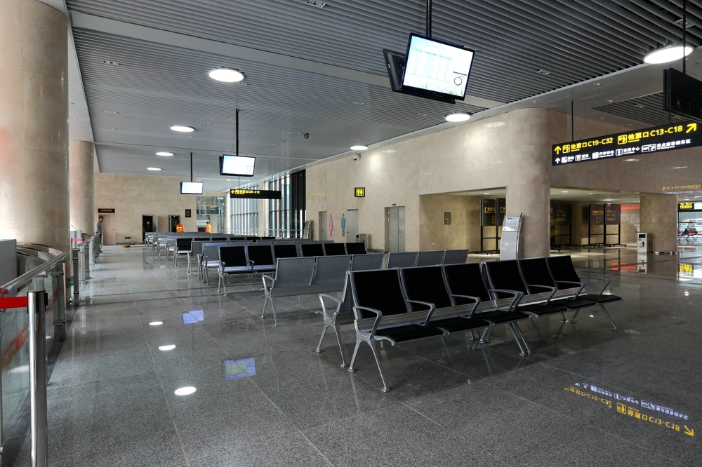 Modern airport waiting area with rows of empty metal chairs and digital signage displaying departure information. Modern airport waiting area with rows of empty metal chairs and digital signage displaying departure information.