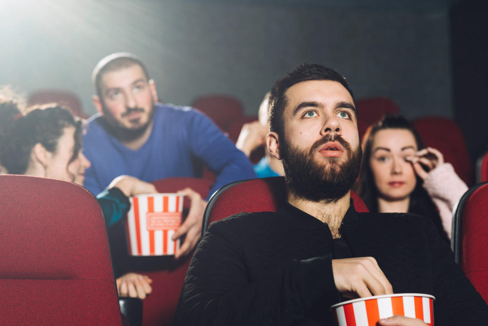 Experiencia de cine tradicional: Hombre viendo una película con amigos, disfrutando de palomitas de maíz.