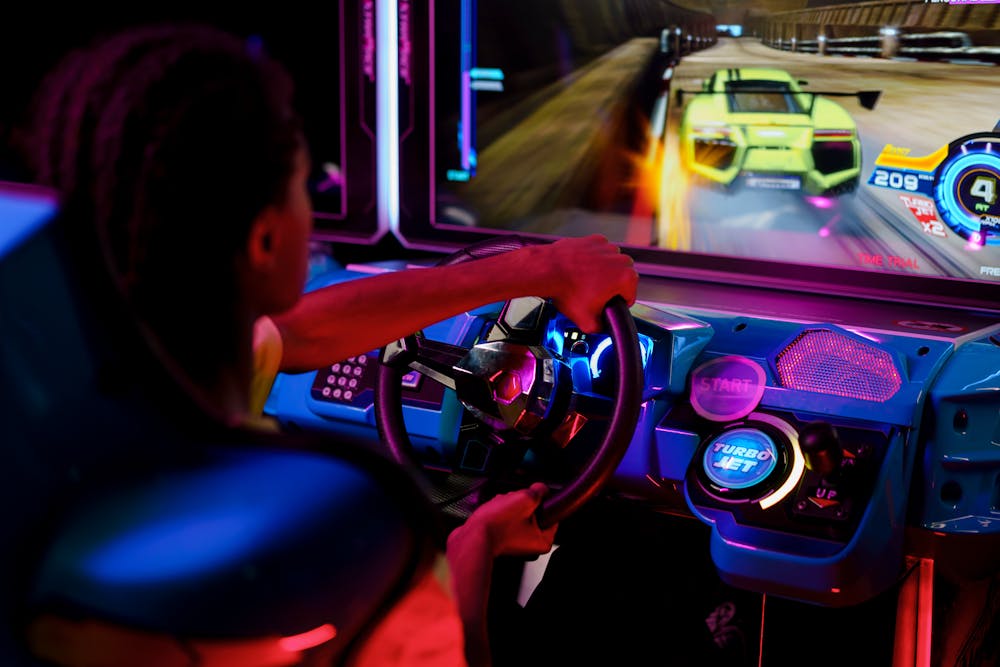 Person playing a car racing arcade game in a neon-lit arcade.