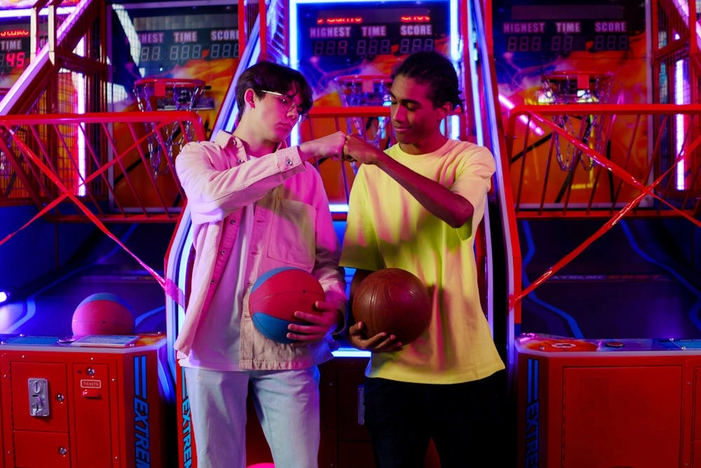 Two young men fist-bumping in front of basketball arcade games. - VRN0.1
