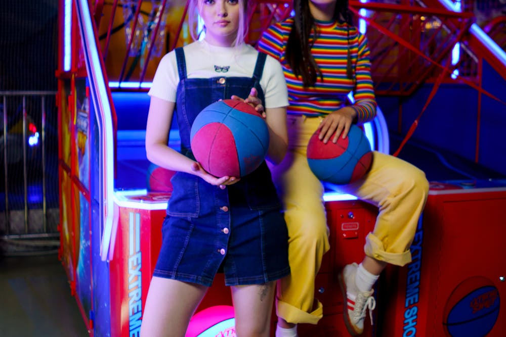 Two girls play a Basketball Game Machine, holding game basketballs.