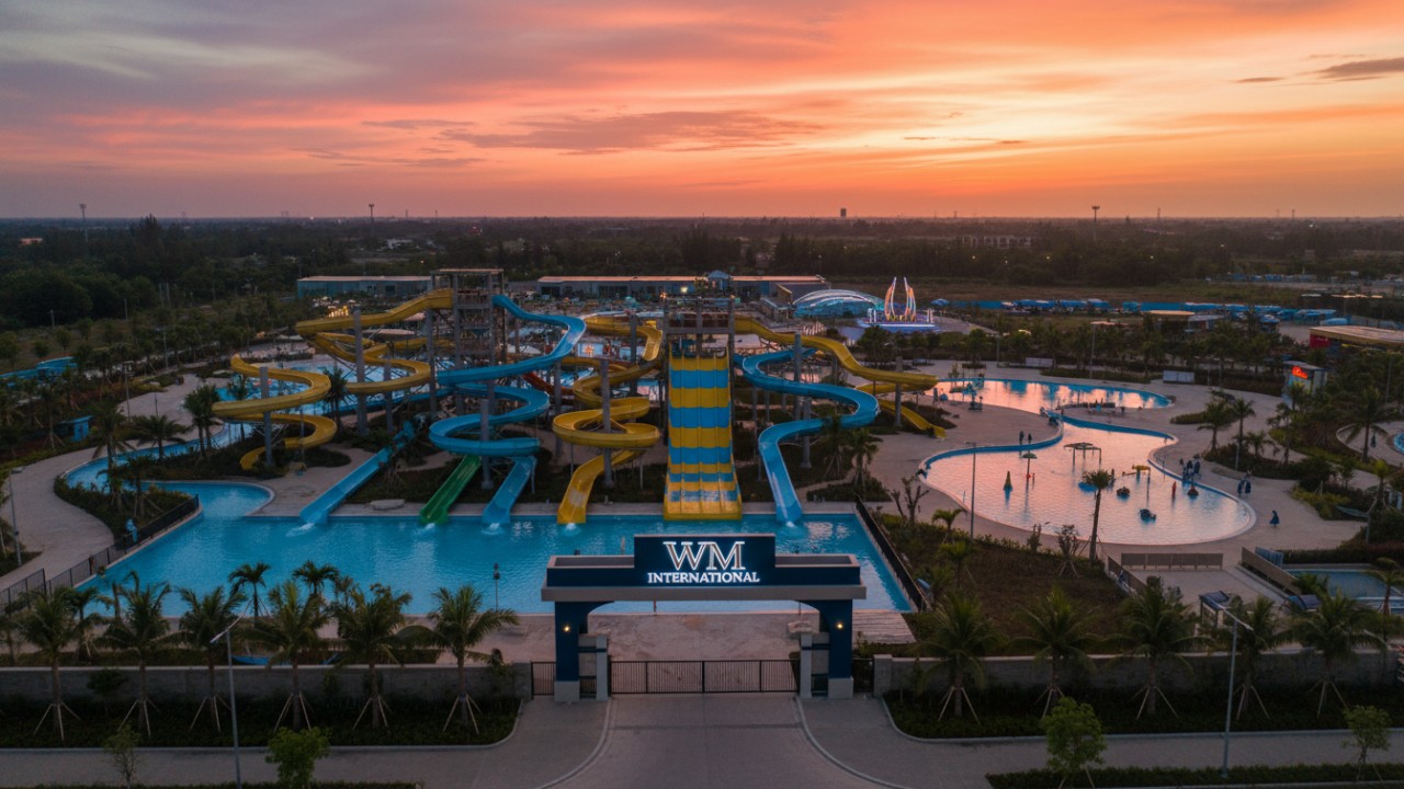 An expansive aerial view of a modern water park at sunset with a large WM International monument sign.