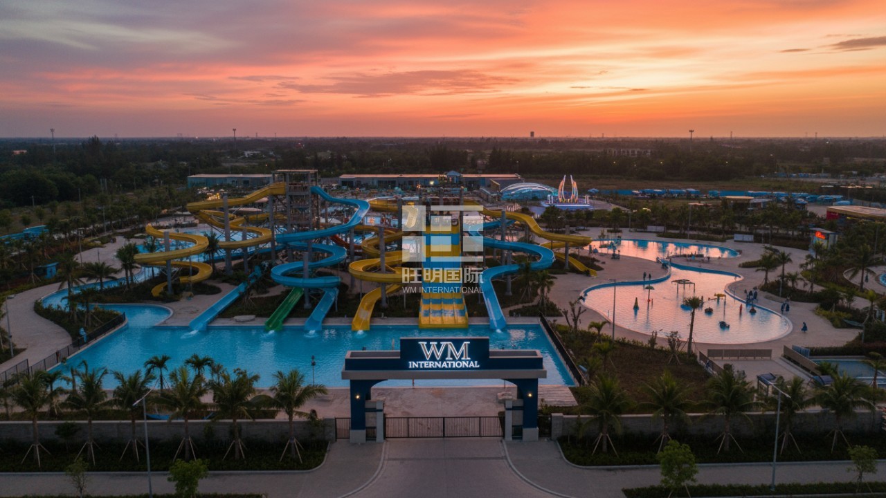 An expansive aerial view of a modern water park at sunset with a large WM International monument sign.
