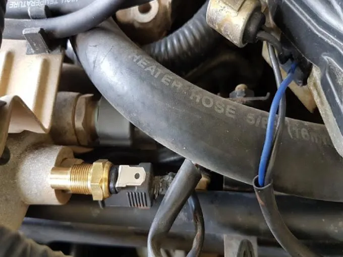 Close-up of car engine bay showing car temperature sensors, specifically a Coolant Temperature Sensor, installed near engine coolant hoses and wiring.