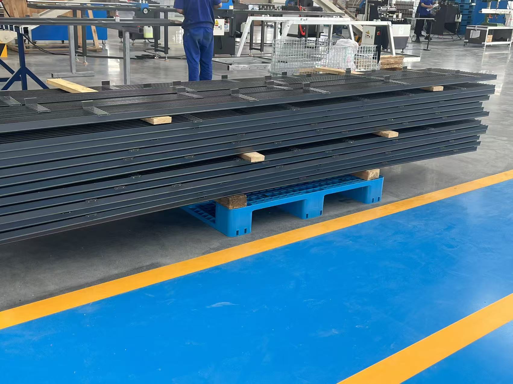 Stack of black metal fence panels on a blue pallet in a factory.