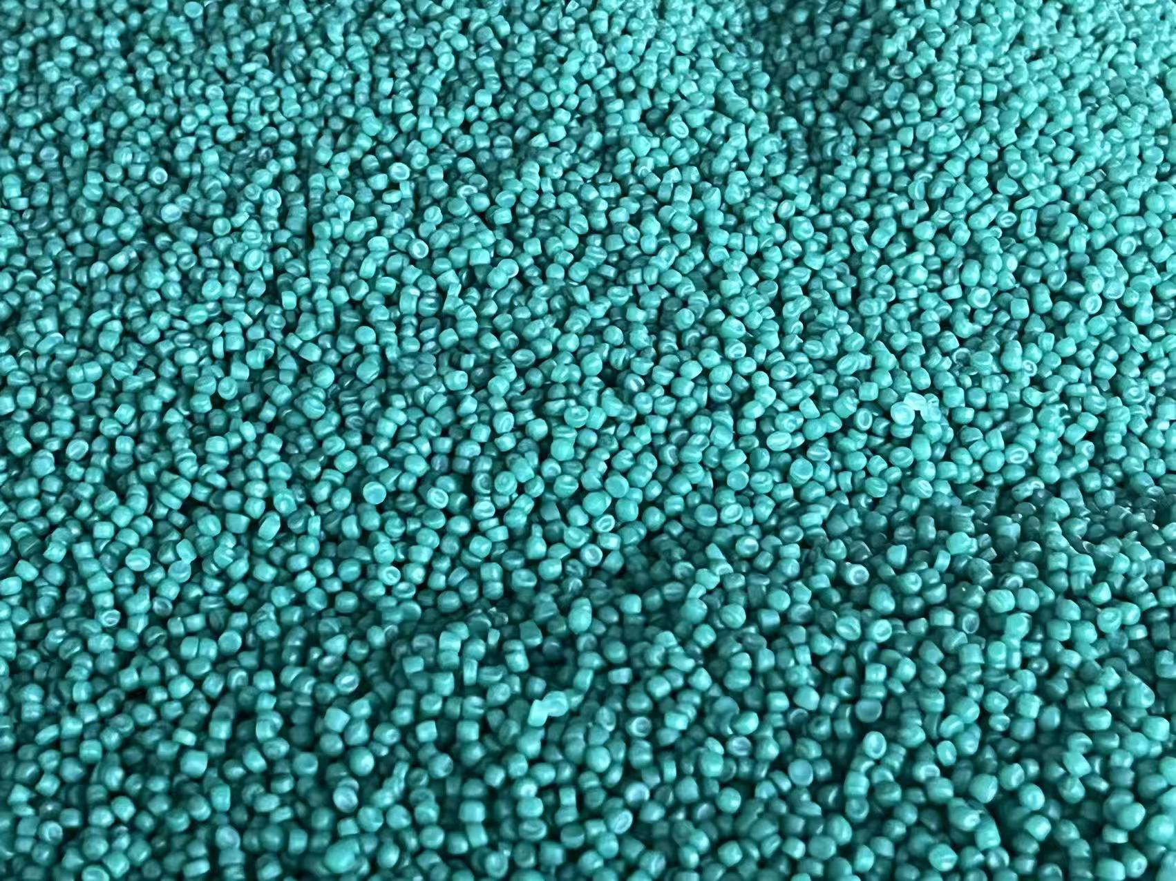 Close-up of a dense pile of small, round green granular PP material pellets.